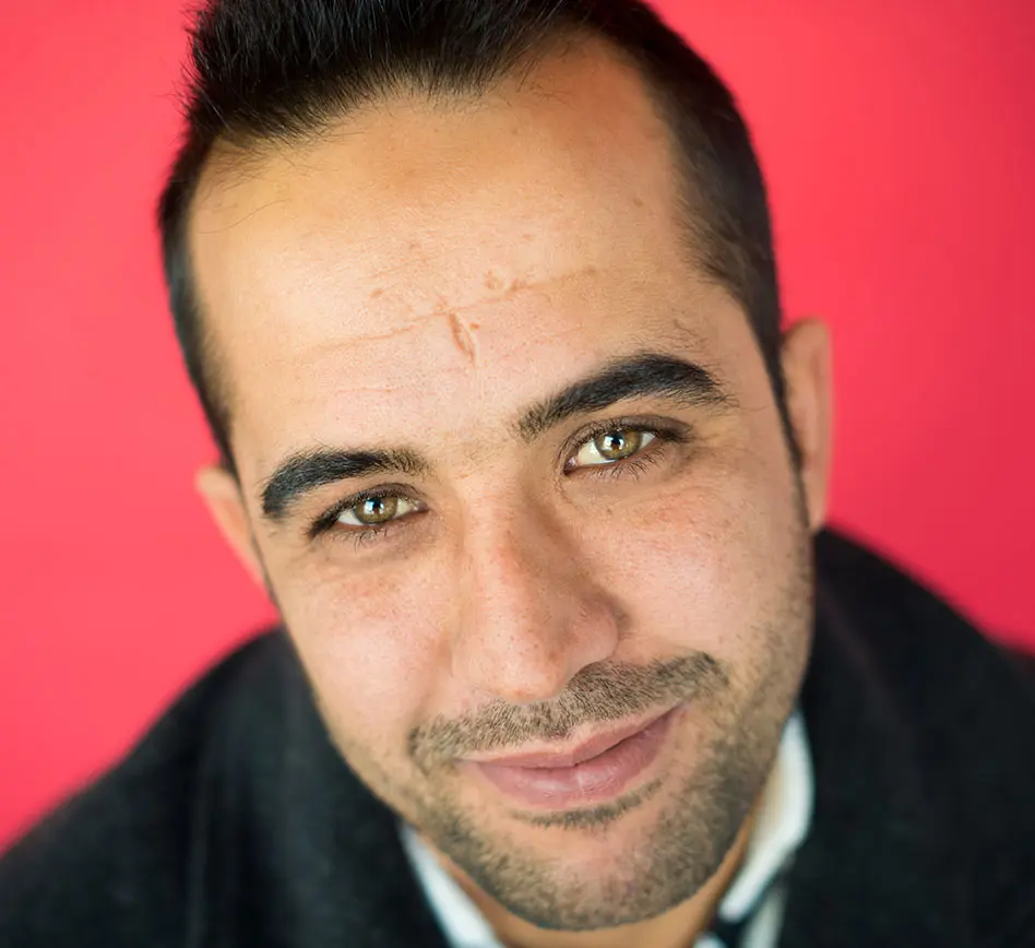 Male Refugee Smiling in Front of Red Background